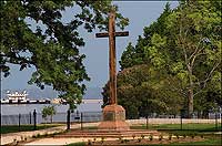 The wooden cross honors the Starving Time dead, scores of whom may be buried on the fenced ridge behind it.